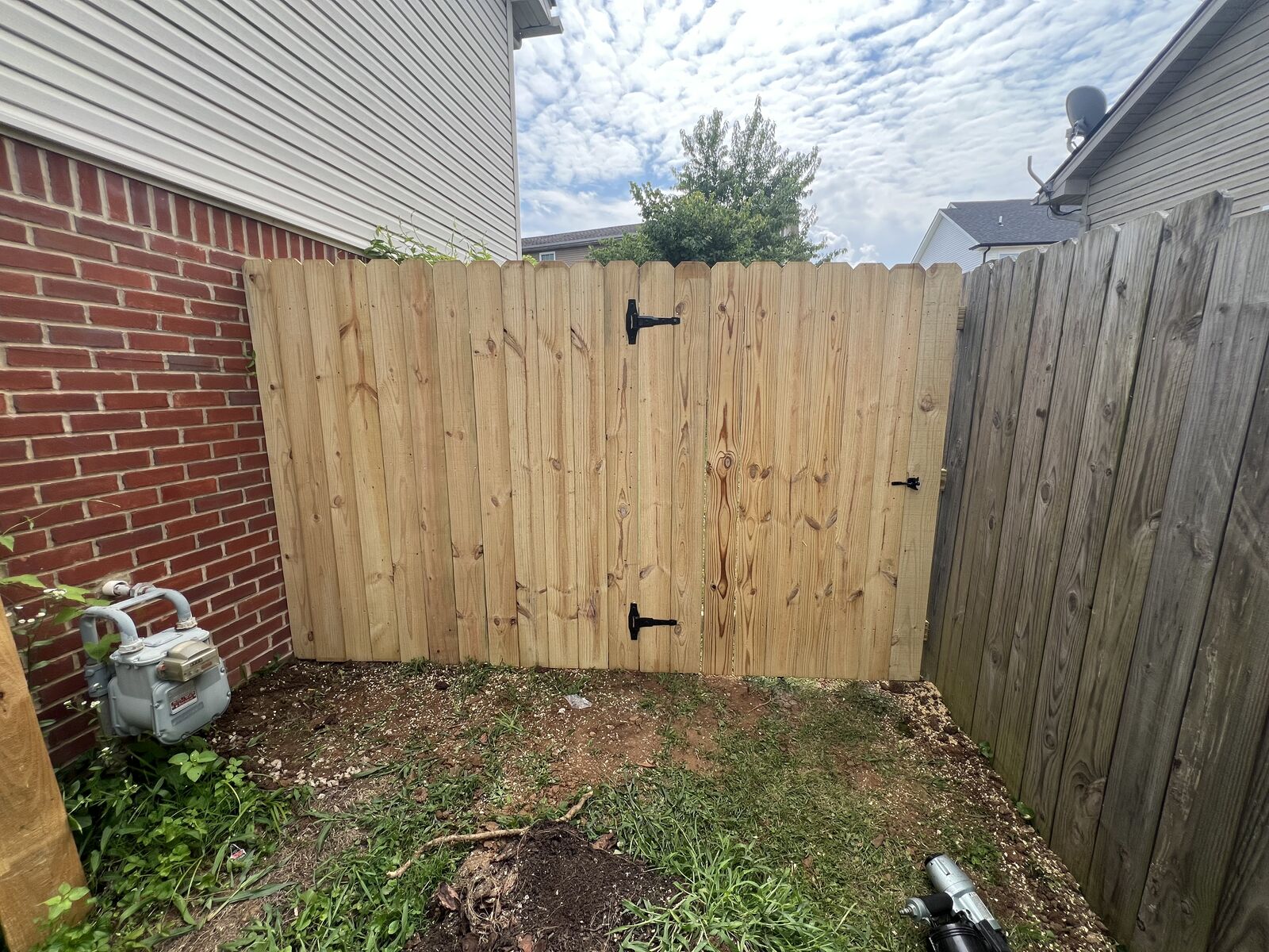 Wood privacy fence with a gate and black hinges beside a brick home